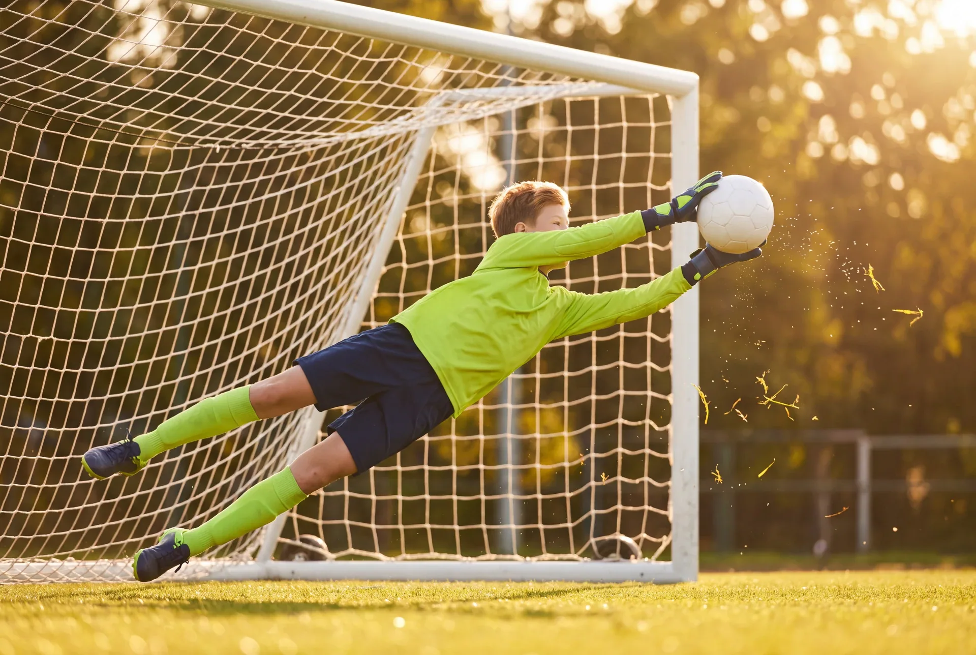 Brankář v limetkovém dresu se v letu natahuje po míči před brankou.